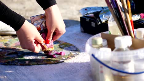 close-up, female hands with bright red manicure. the artist squeezes some burgundy paint from a tube