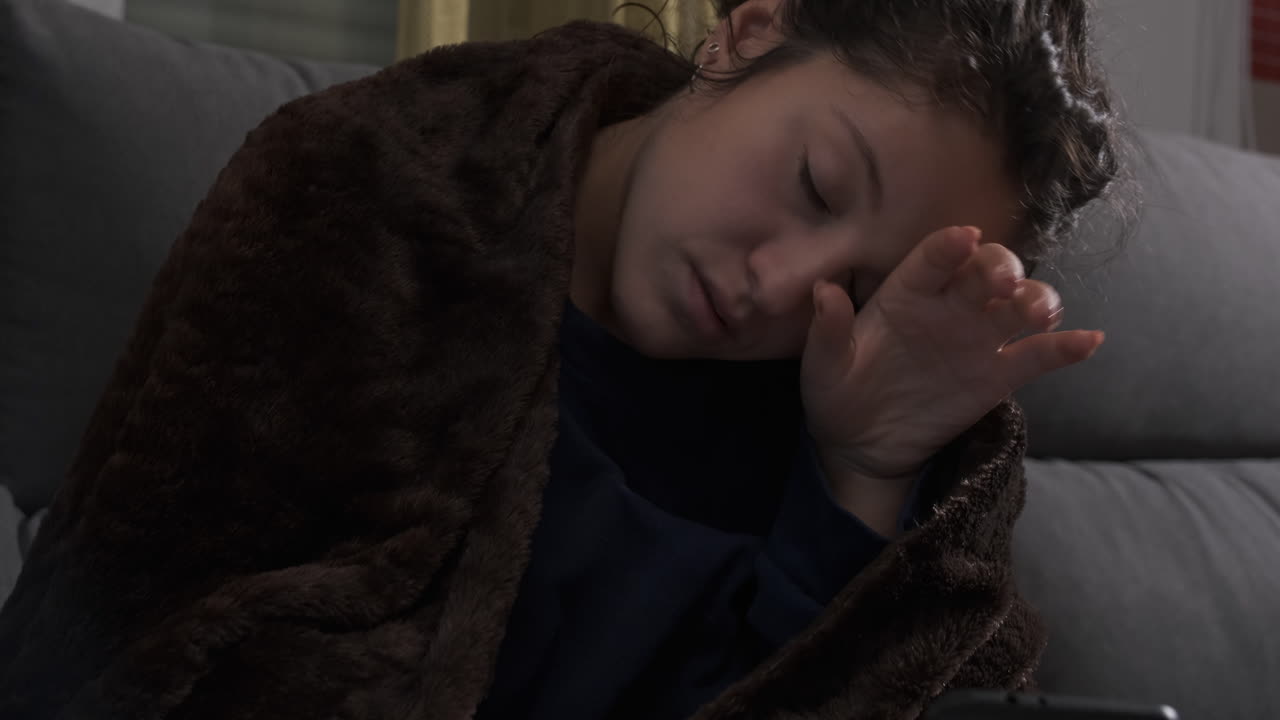 Young woman sick on the couch at home, looking for medicine in her mobile phone.