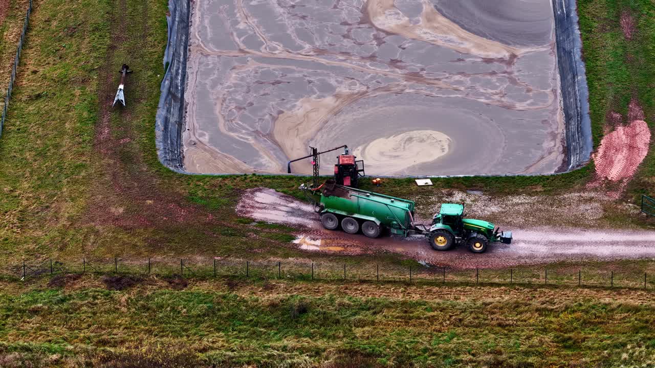 Vista aerea di un grande scavo rettangolare con lavori di sterro e attrezzature intorno al sito, un trattore fa retromarcia con una cisterna d'acqua