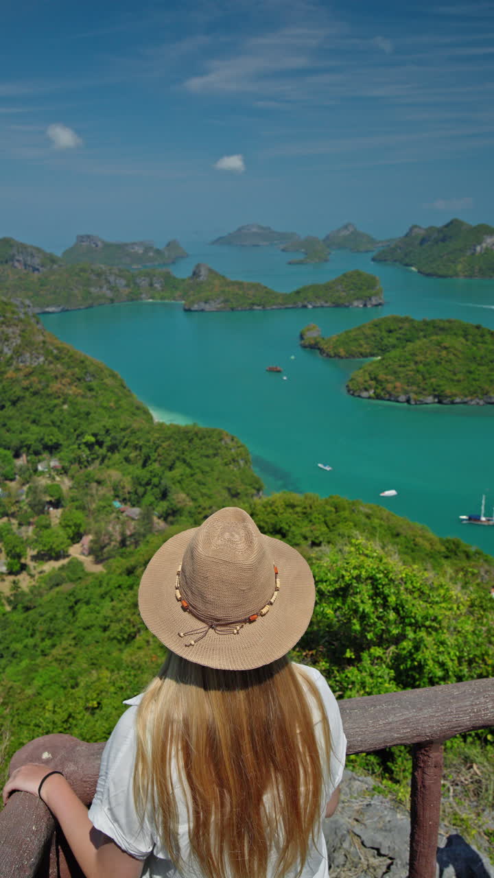 Adolescente com chapéu de palha em um mirante panorâmico, observando o mar turquesa e ilhas tropicais, em um momento de viagem tranquilo com paisagem de ilha cênica e atmosfera de verão. Filmagem 4K de alta qualidade.