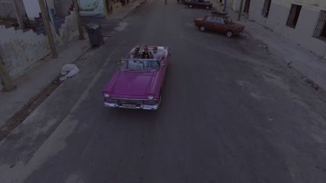 rising drone aerial of a group of tourists riding in a classic old car through the streets of havana cuba