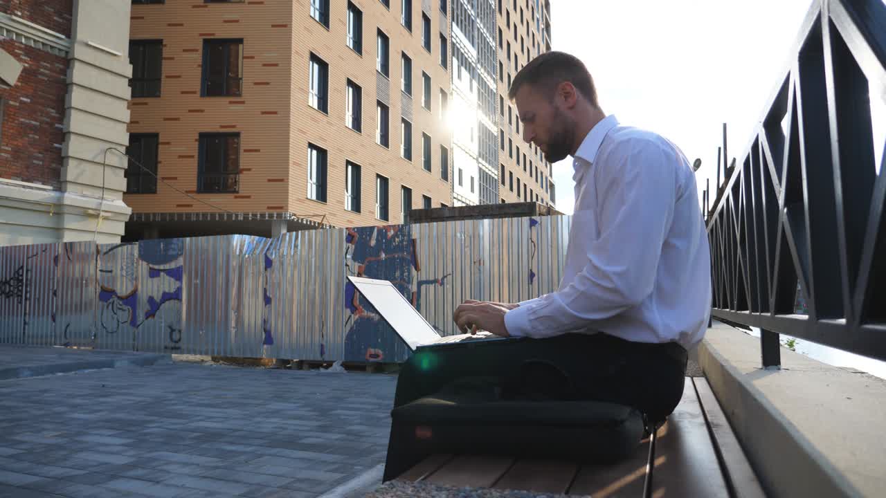 Imprenditore di successo lavora al notebook seduto su una panchina in città. Manager fiducioso digita testo sul laptop all'aperto. Giovane uomo d'affari usa il computer in città. Concetto di affari e finanza. Primo piano.