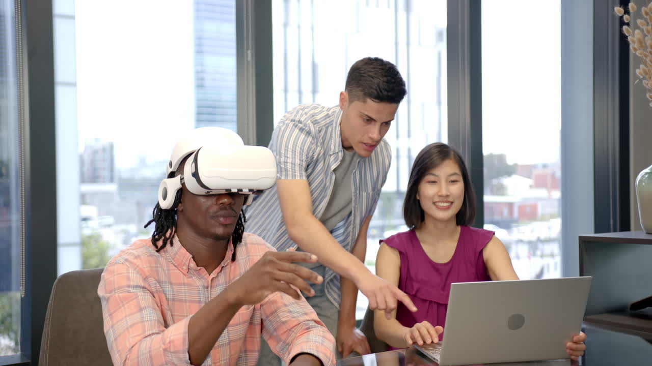 Using VR headset, man interacting while colleagues assist with laptop in office