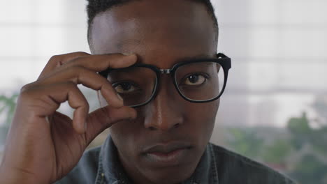 close up portrait of young african american business student intern man puts on glasses looking serious at camera