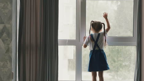 chica en vestido de denim ondas de la mano mirando fuera de la ventana grande