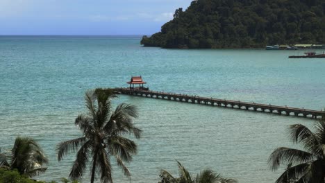 un muelle con un pequeño techo rojo al final, en el océano con palmeras