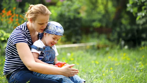 Boy-playing-with-toy-car-sitting-on-moms-lap-outdoor