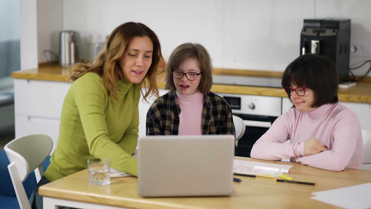 la maestra enseña a las niñas con discapacidades a usar una computadora portátil en la cocina