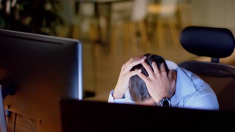 Tired-biracial-businessman-at-desk-with-computers-in-office-at-night,-slow-motion