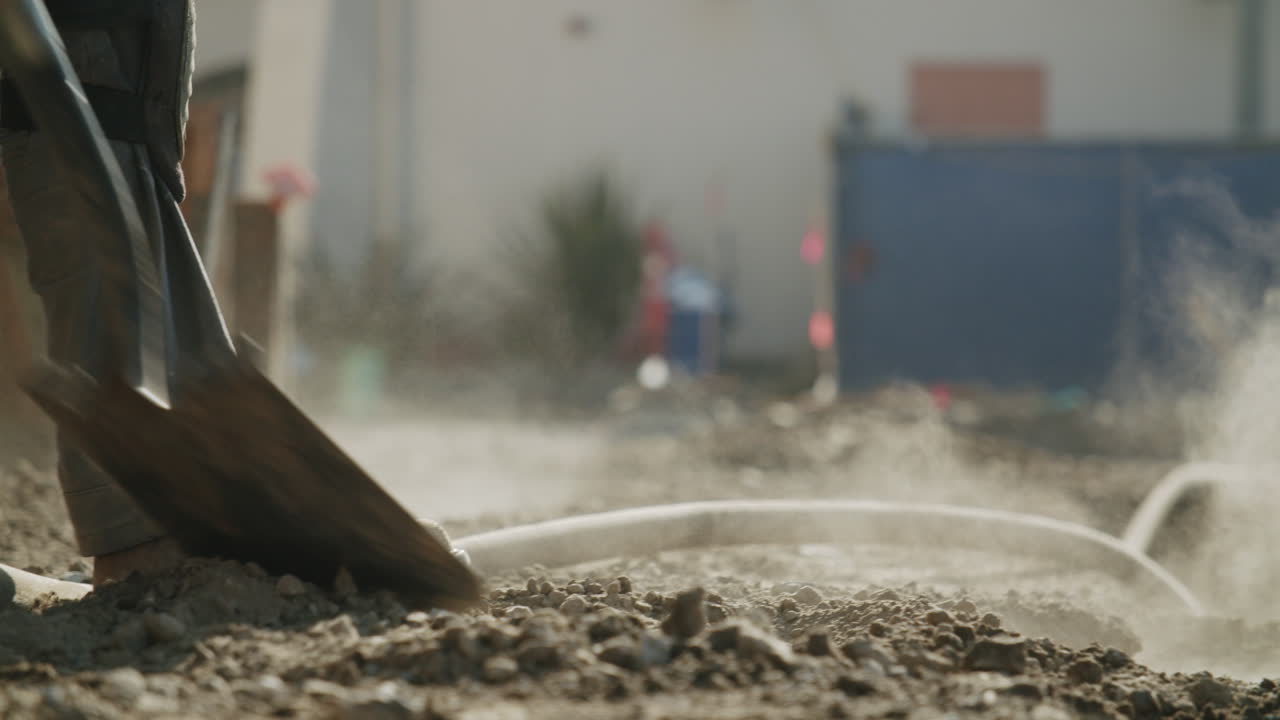 Worker Digging Dirt with a Shovel on a Dusty Construction Site