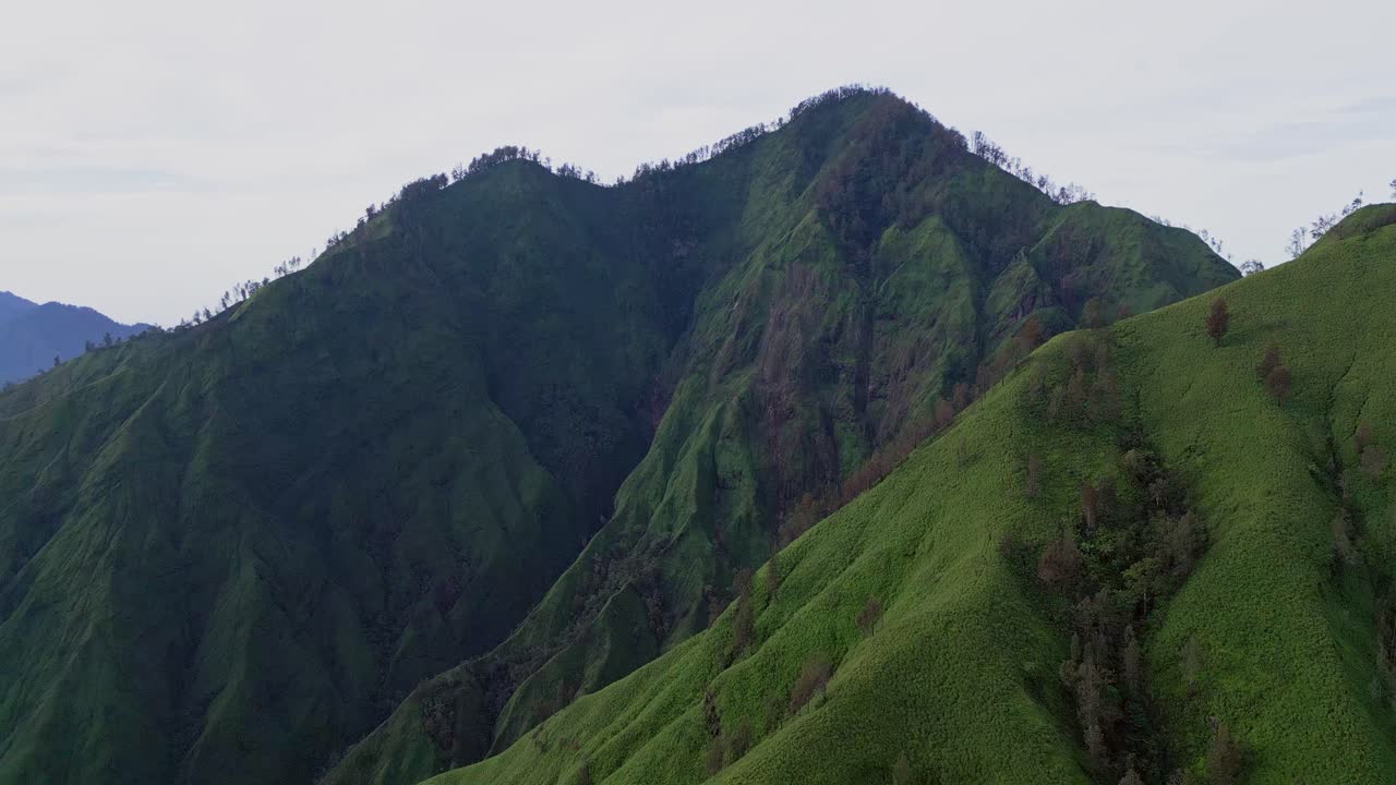 Mount Abang’s vibrant green ridges shine under soft morning skies while Mount Agung rises beyond, captured in cinematic aerial drone footage during a quiet Bali sunrise.