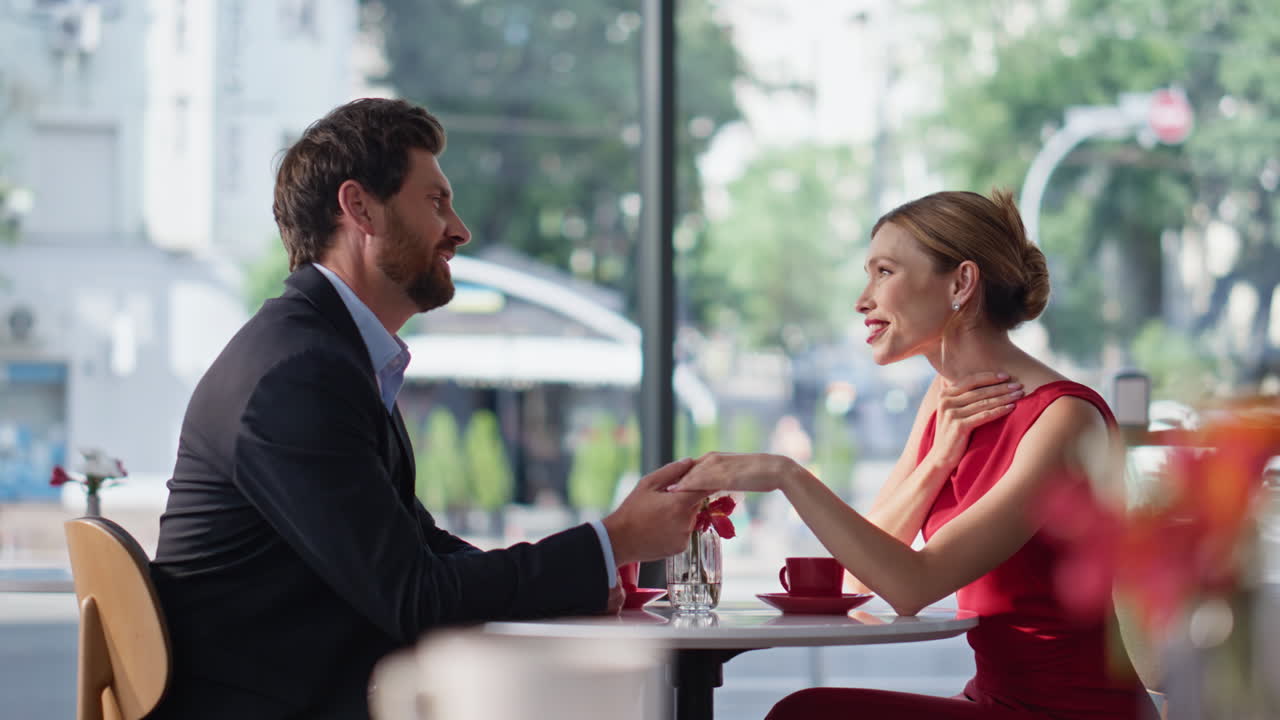 Lovely couple holding hands sitting cozy cafe. Smiling man talking beloved woman