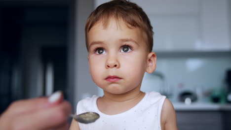 beautiful child talks instead of eating. mom gives him spoon but he turns away saying something.