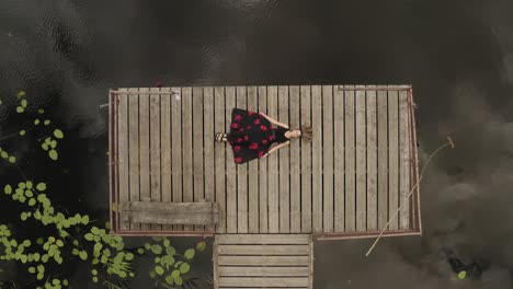 Zoom-out-of-lonely-girl-sleeping-on-wooden-path-near-dark-lake