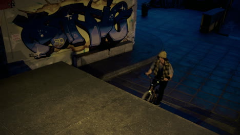 active man jumping bmx bicycle through steps at skate park with graffiti wall.