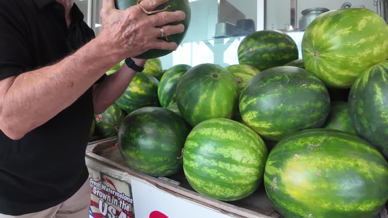 elderly man tests a watermelon for ripeness at a grocery store