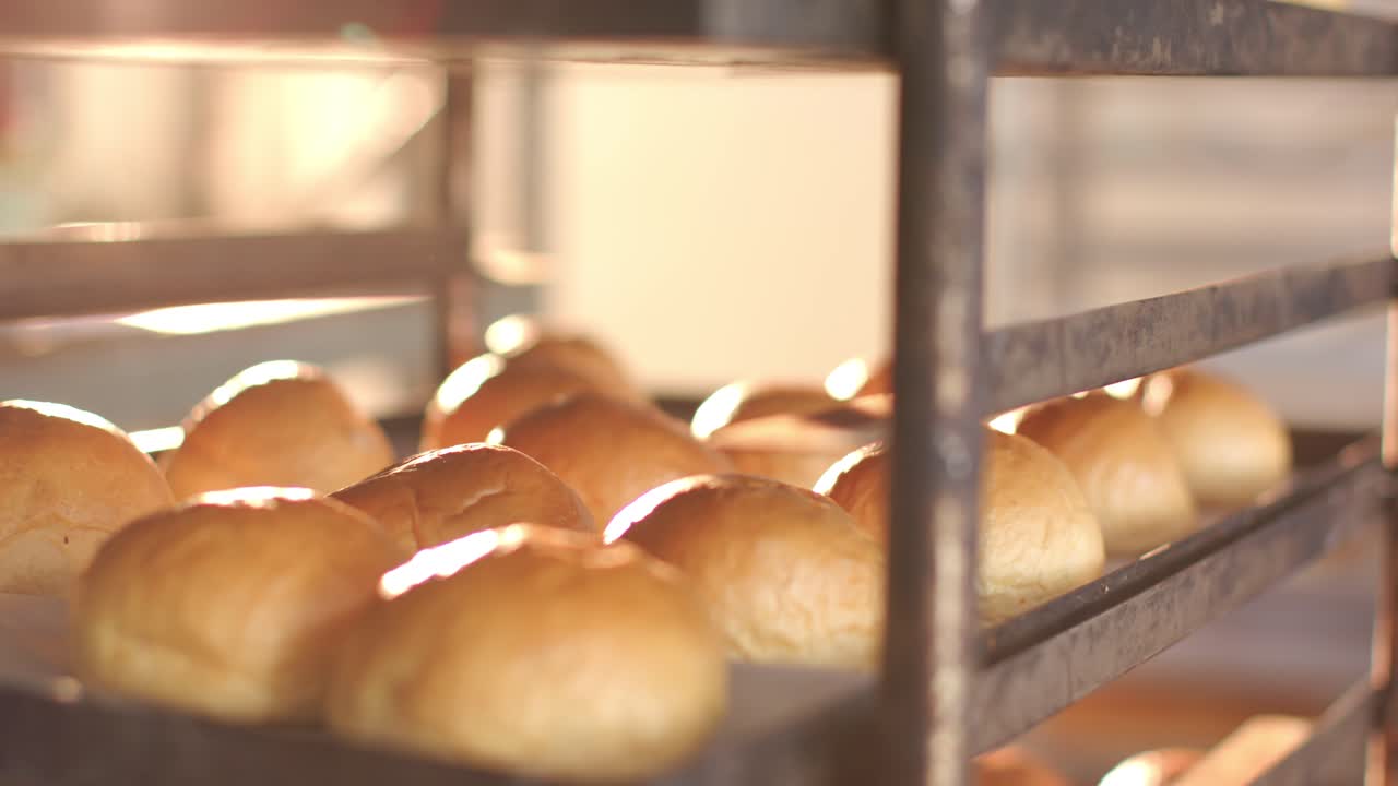 La telecamera esegue una panoramica attraverso i vassoi su una rastrelliera metallica in una panetteria, rivelando panini lucidi e mostrandone la consistenza.