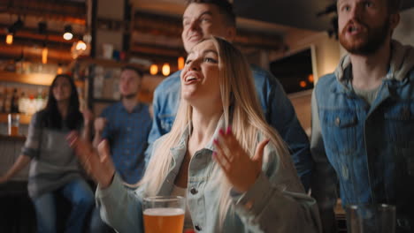 Portrait-of-a-blonde-female-fan-watching-football-in-a-bar-with-friends.-football-hockey-basketball-sports-games.