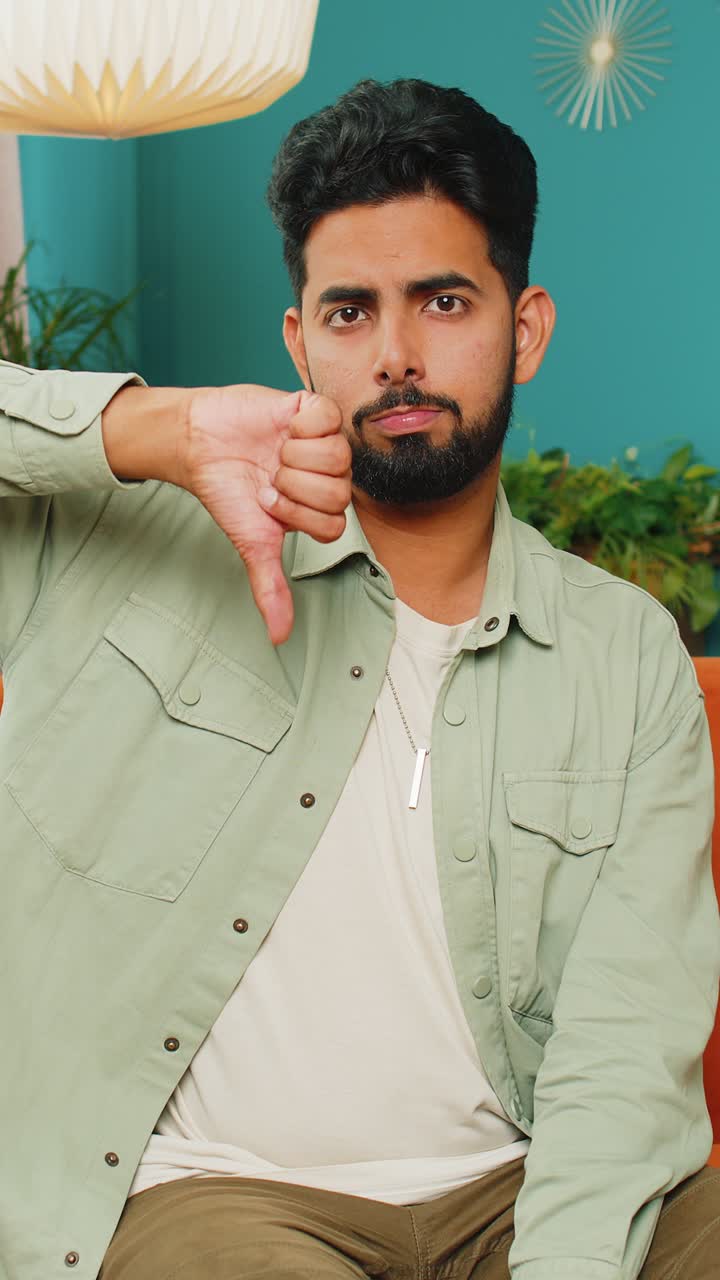 Upset arabian man showing thumbs down dislike bad work disapproval dissatisfied feedback at home