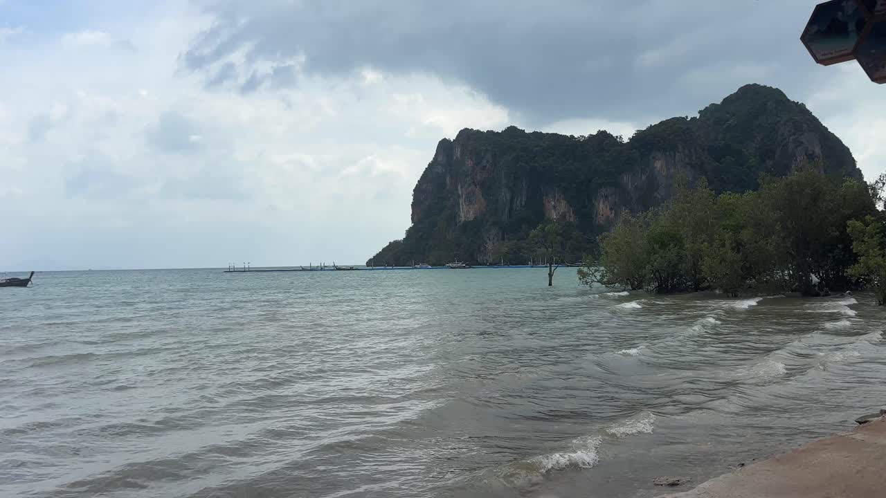 Acqua di mare calma si estende lungo Railay Beach a Krabi con una piccola barca che galleggia al largo, dolci onde vicino alla riva e scogliere calcaree che incorniciano una tranquilla costa tropicale.
