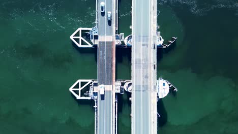 Landscape-view-of-car-vehicles-driving-along-freeway-main-road-over-Swansea-channel-inlet-river-bridge-wharf-pier-Belmont-Australia-transport-drone-aerial