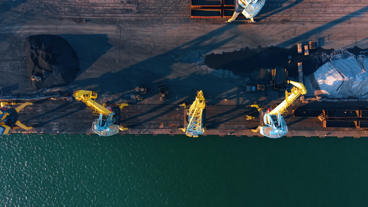 Symmetrical top view of three portal cranes on pier. Aerial direct overhead shot of heavy industrial cranes and turquoise water