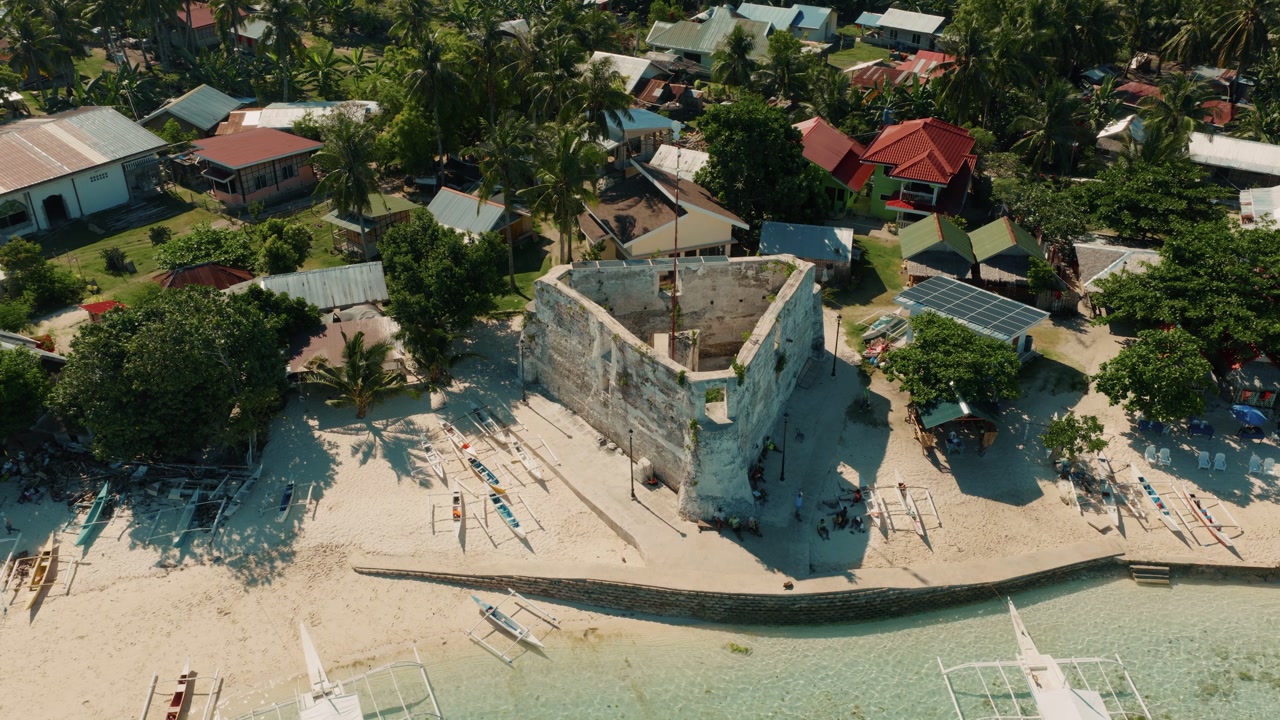 Aerial of historic stone watchtower near sandy beach and coastal village Pamilacan Island Bohol Philippines, establishing