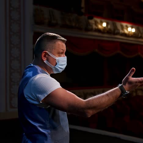 actor on stage. man in medical mask is talking to empty auditorium. speaker in protective mask during the rehearsal. rear view