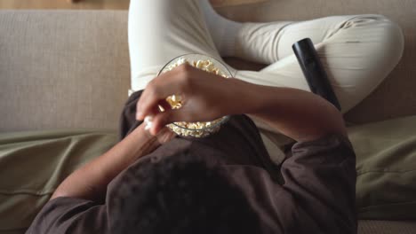 hombre irreconocible comiendo palomitas de maíz y viendo televisión en el sofá