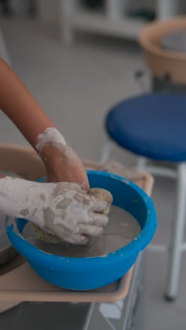 close-up of hands working with clay and water in a pottery studio