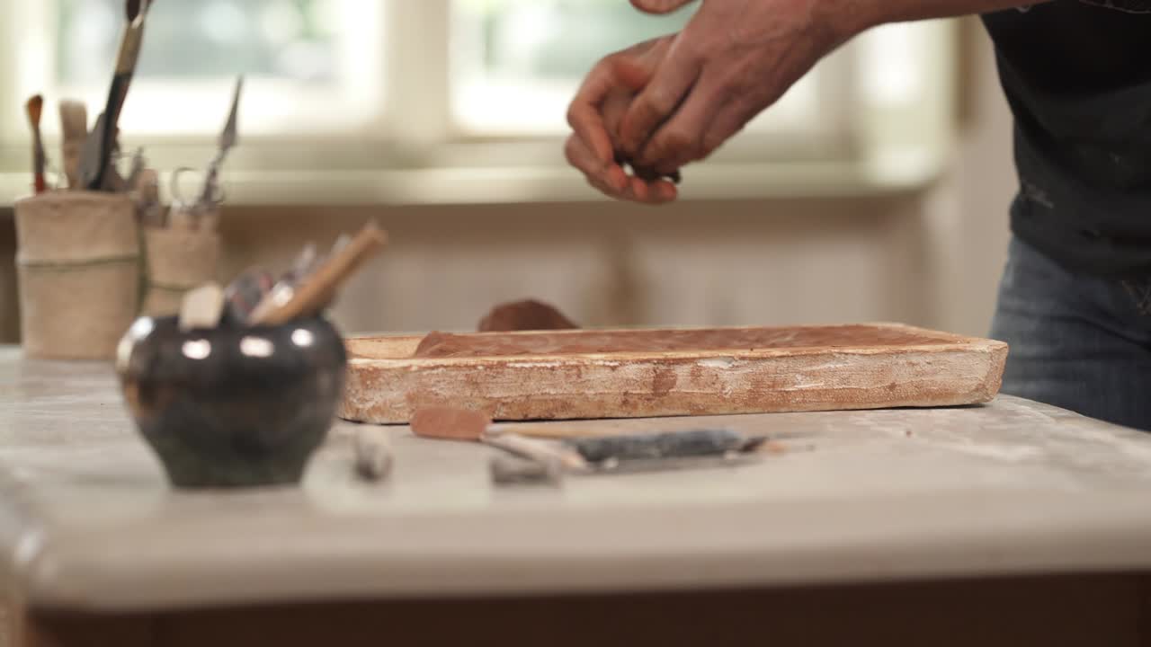 Close-up of male ceramist molding clay and carefully placing it into wooden form to shape the clay. Exclusive handmade ceramic product creation. Selective focus shot