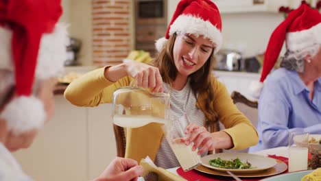 Caucasian-woman-in-santa-hat-pouring-drink-in-glass-of-senior-man-while-sitting-on-dining-table-and-