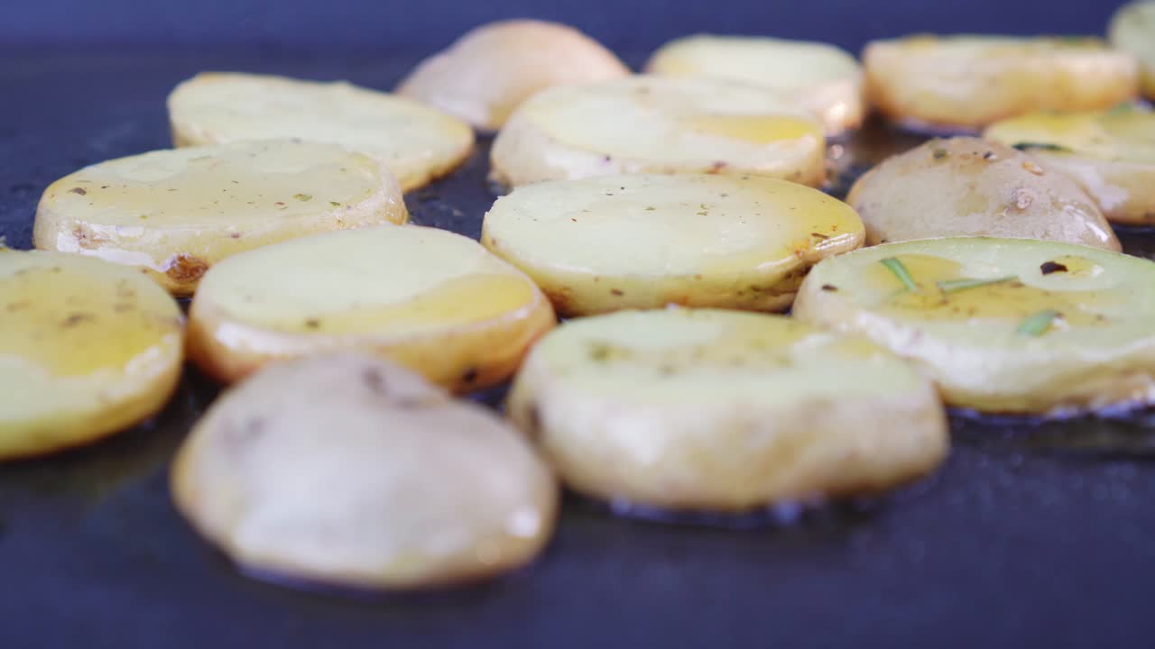 Sliced potatoes on grill pan, putting spice on, closeup