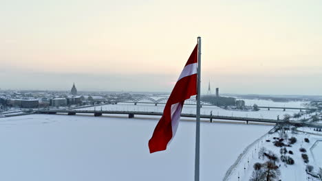 aerial orbiting shot of latvian flag and snowy daugava river during cold winter day in riga