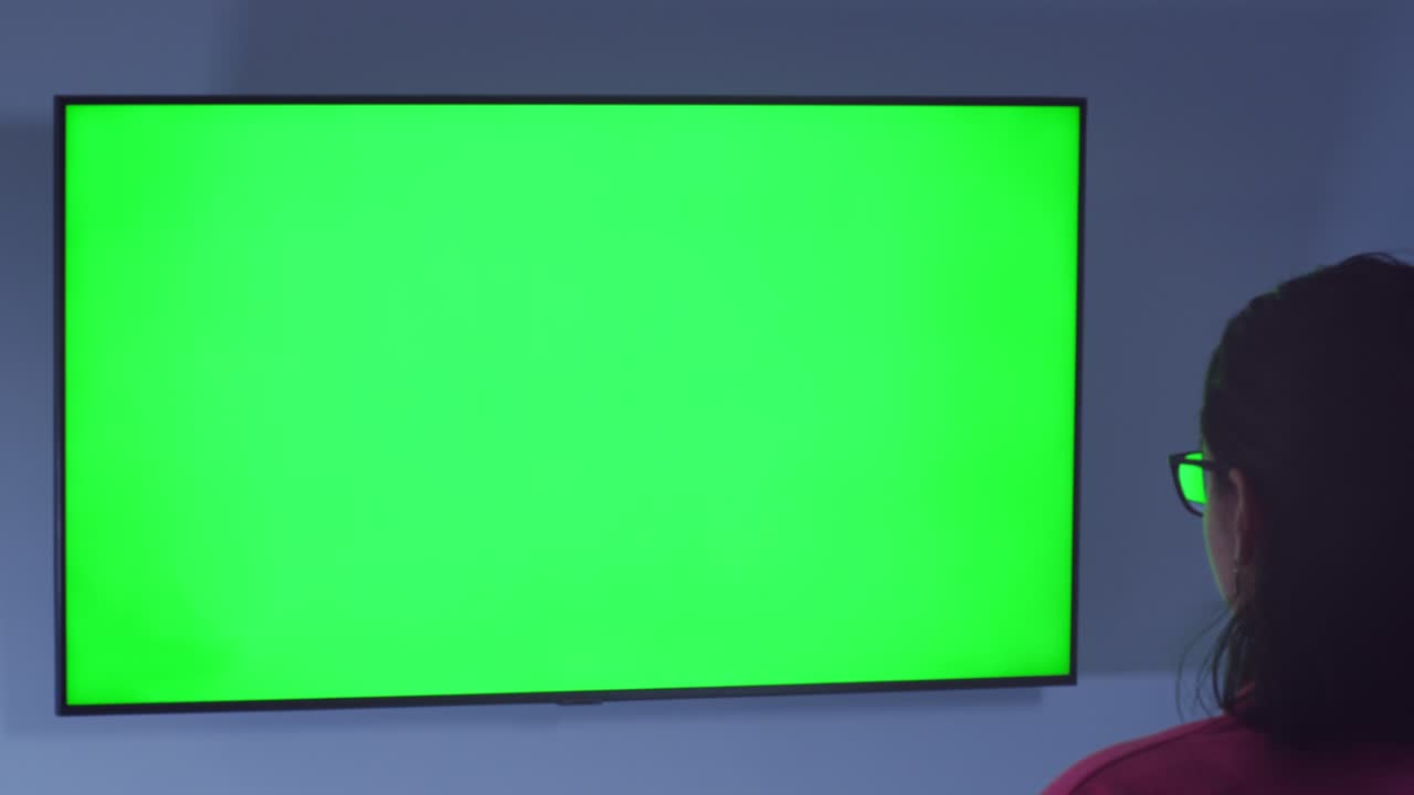 Brunette girl watching the news in the evening sitting in front of the TV, rear view, chromakey