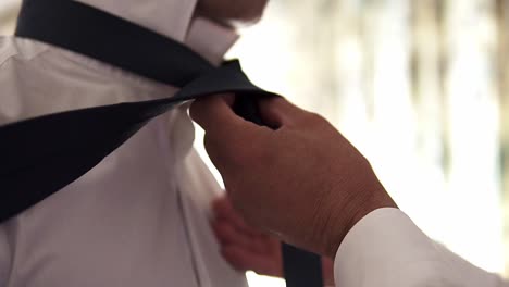 slow motion handheld close up shot of a groom getting his tie tied by another person before his wedding with his wife