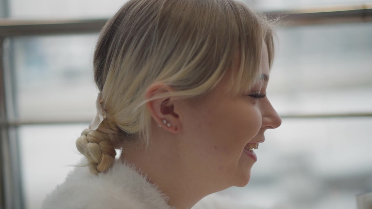 Primo piano di profilo di una donna che gira la testa con un movimento sottile e respiro rilassato vicino a una finestra luminosa, passando da un'espressione neutra a un sorriso gentile con gli occhi chiusi nella luce soffusa interna.
