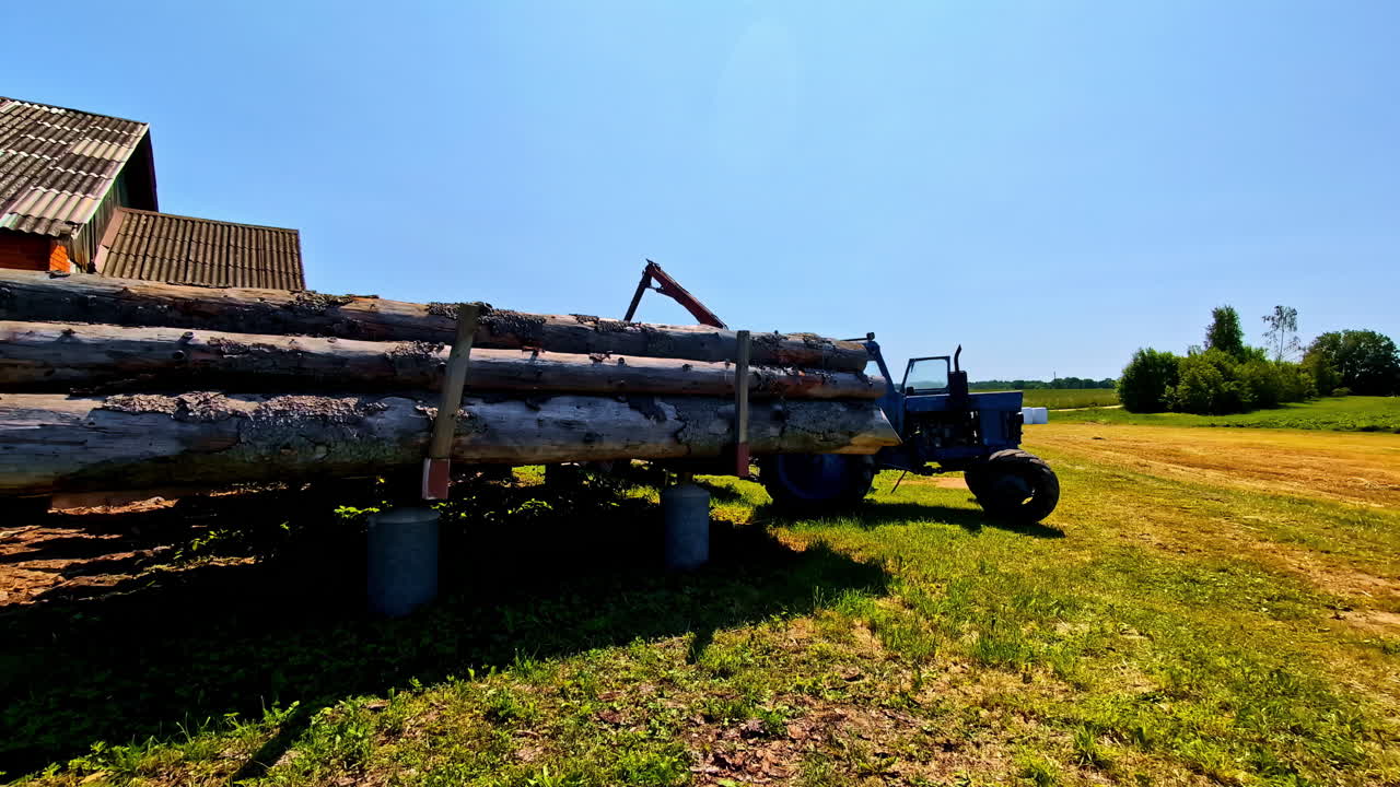 Long Timber Logs Loaded on Blue Tractor Trailer in Sunny Open Field Setting
