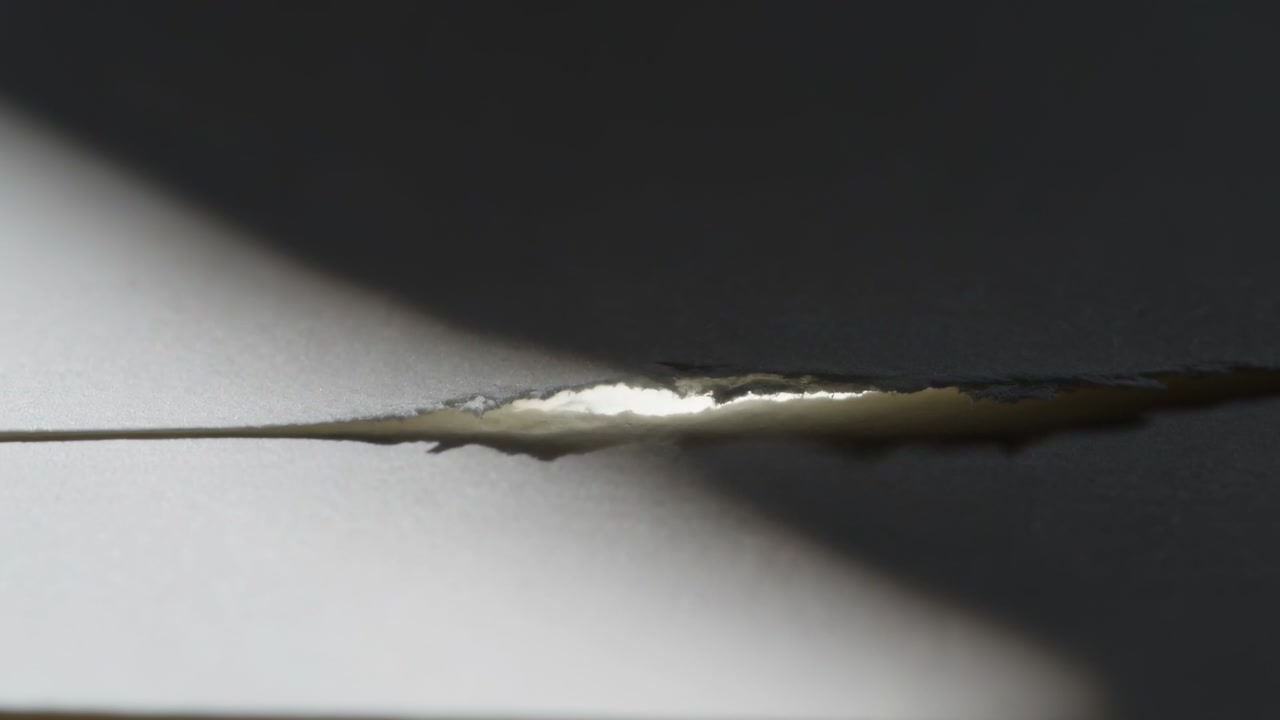 Shifting light sweeping torn slit on white panel indoors, showing edges, filament as shadow passes