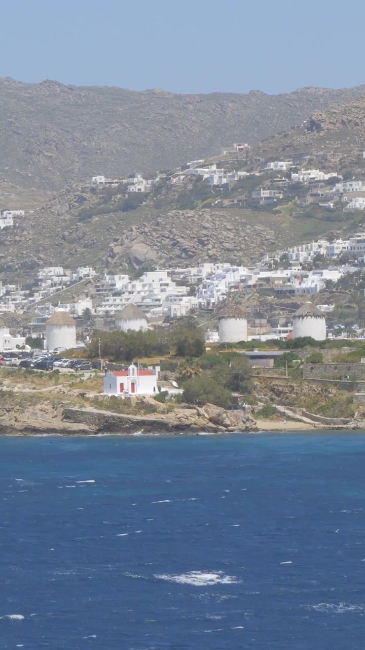Vista verticale che cattura i tradizionali mulini a vento di Mykonos, Grecia, che si ergono sullo sfondo del Mar Mediterraneo.