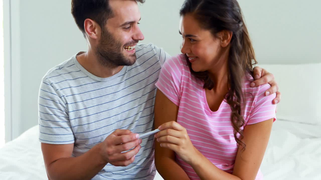 Happy couple looking at pregnancy test on bed in bedroom