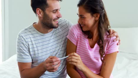 happy couple looking at pregnancy test on bed in bedroom
