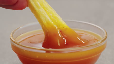 hand dipping french fries into sauce