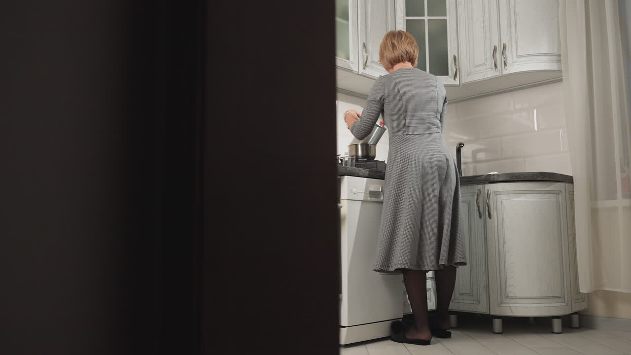 Woman seen from behind dancing and cooking in modern kitchen with a relaxed, joyful vibe, she stirs pot and moves with rhythm in stylish, well-lit kitchen
