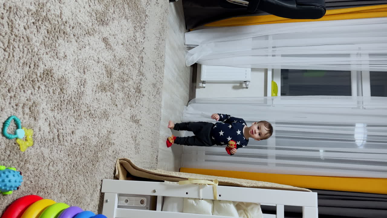 Active happy toddler running by the room in one sock. Kid holds another sock in hands and shoves it to mouth. Vertical screen.