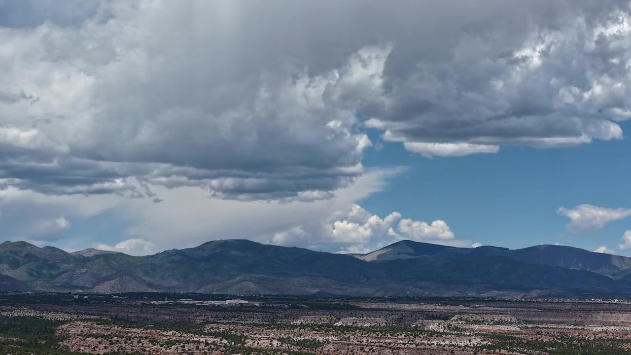 Timelapse con drone 4K UHD: pesanti formazioni di nubi cumuliformi si accumulano su catene montuose distanti e vaste mesas aride. La luce mutevole cattura i cambiamenti dinamici del tempo e del clima atmosferico.