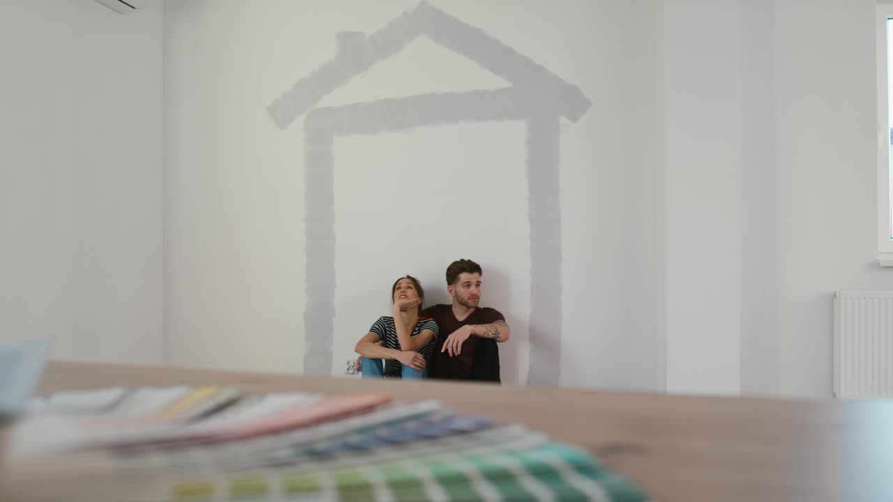 una pareja caucásica descansando después de pintar la pared de la nueva casa.