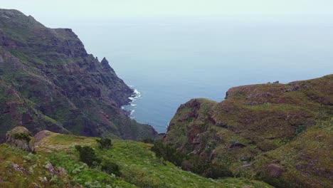 Epic-mountain-cliffs-and-coastline-reveal-of-Roque-de-Taborno-with-Caucasian-male-hiking-in-Tenerife,-Canary-Islands,-Spain---aerial-view