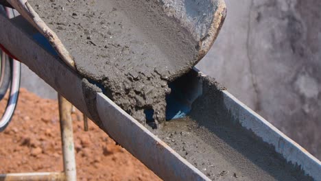 close up concrete flowing and pouring from mixer cement truck pours liquid concrete in works building at construction site