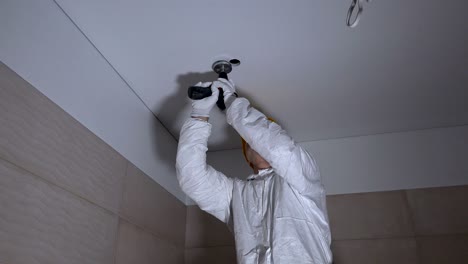 hombre constructor de pie en la escalera y perforar agujeros en el techo